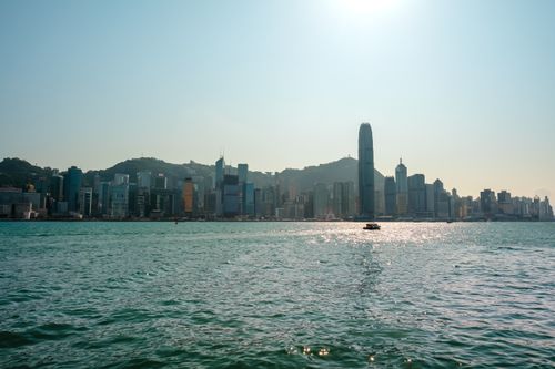 Free Scenic view of Hong Kong skyline across Victoria Harbour with sunlight reflecting on the water. Stock Photo