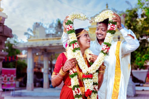 Smiling Newlyweds in Traditional Clothing Standing with Garland in Heart Shape
