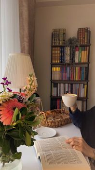 Enjoy a peaceful moment reading with coffee and fresh flowers in a cozy study nook.