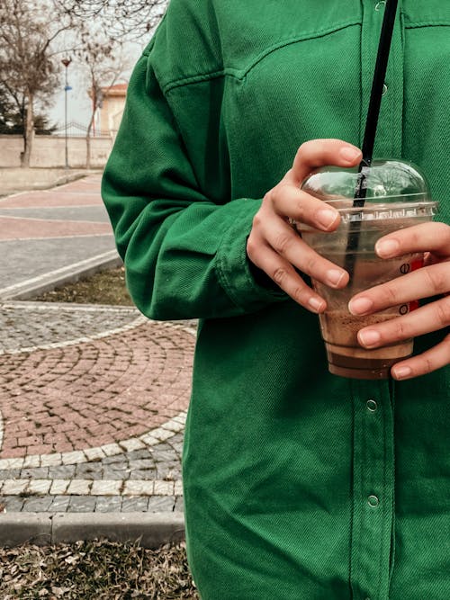 Person in Green Coat Holding Takeout Coffee
