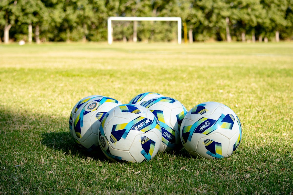 Tre palloni da calcio di diverse misure sull'erba davanti alla porta