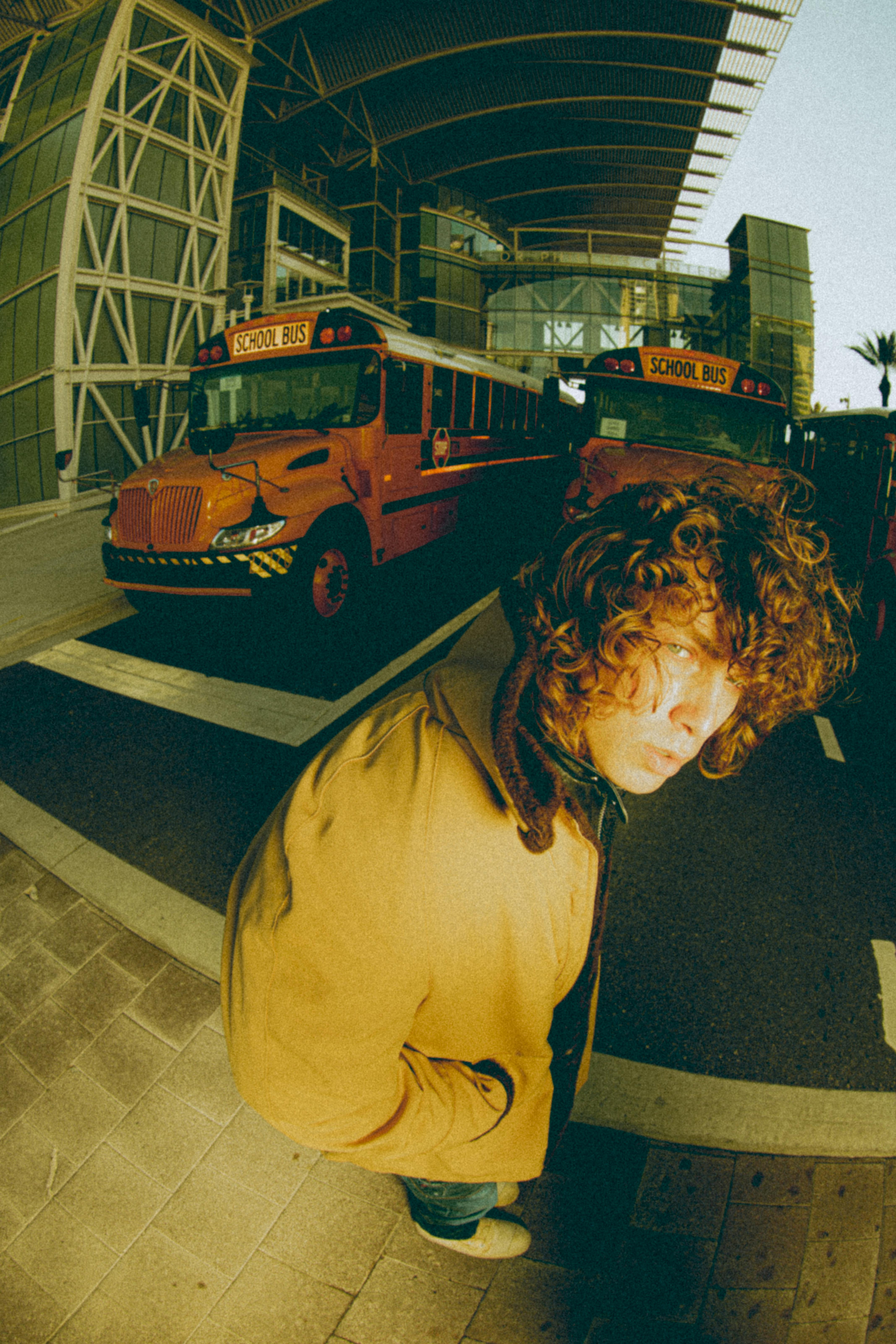 Artistic urban portrait featuring school buses and a modern city backdrop, captured with a fisheye lens.