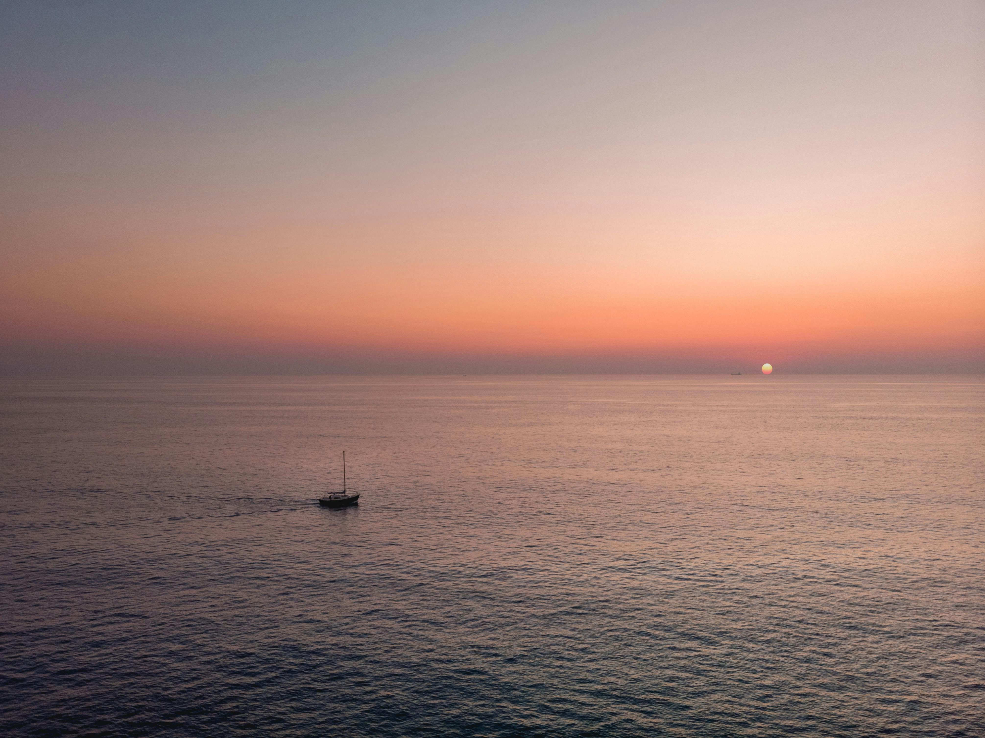 A serene sunset over the calm sea near Valletta, Malta, featuring a lone yacht.