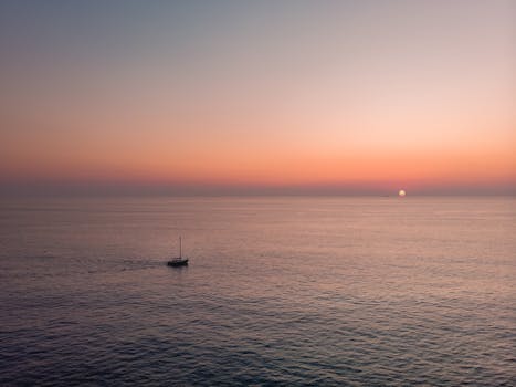 A serene sunset over the calm sea near Valletta, Malta, featuring a lone yacht.