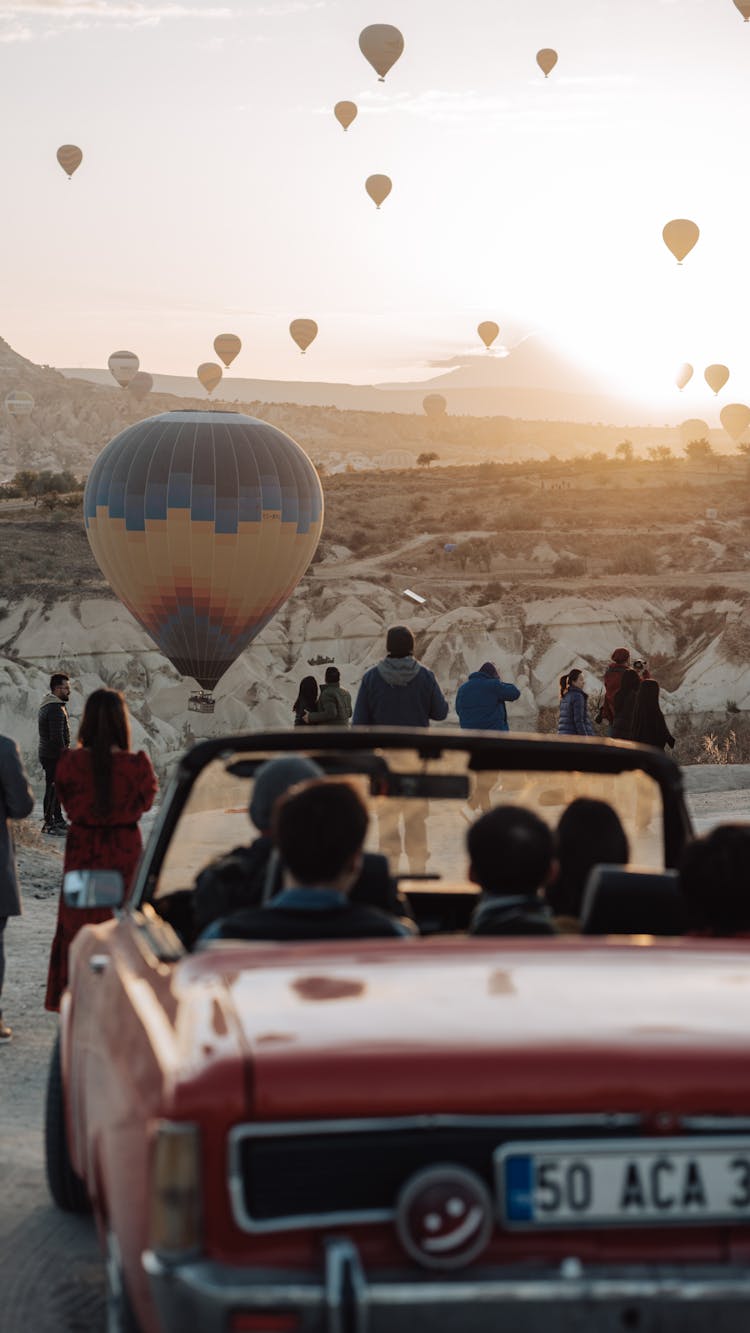 Cabriolet And People Watching Balloons Flying Over Cappadocia At Sunrise