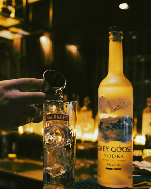 Free A hand pours vodka into a glass with ice at a dimly lit bar, featuring a Grey Goose bottle. Stock Photo