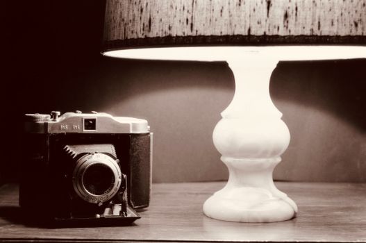 A classic vintage camera and elegant lamp arranged in a sepia-toned nostalgic setting.