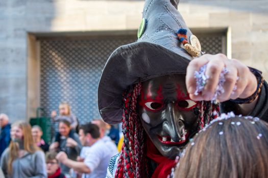 Masked individual in a witch costume celebrating at a parade in Stuttgart, Germany.