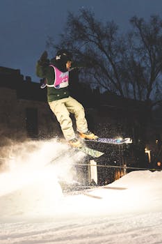 Dynamic shot of a skier performing a freestyle trick at night in a snowy urban setting.
