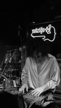 A musician in a dark indoor space plays a keyboard under a neon light sign.