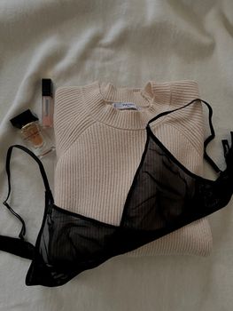 Flat lay with lingerie, folded sweater, and cosmetic vials on a soft white background.