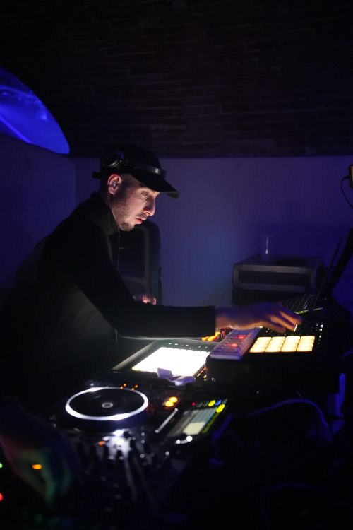 Free DJ performing with sound mixer and DJ controller in a dimly lit nightclub setting. Stock Photo