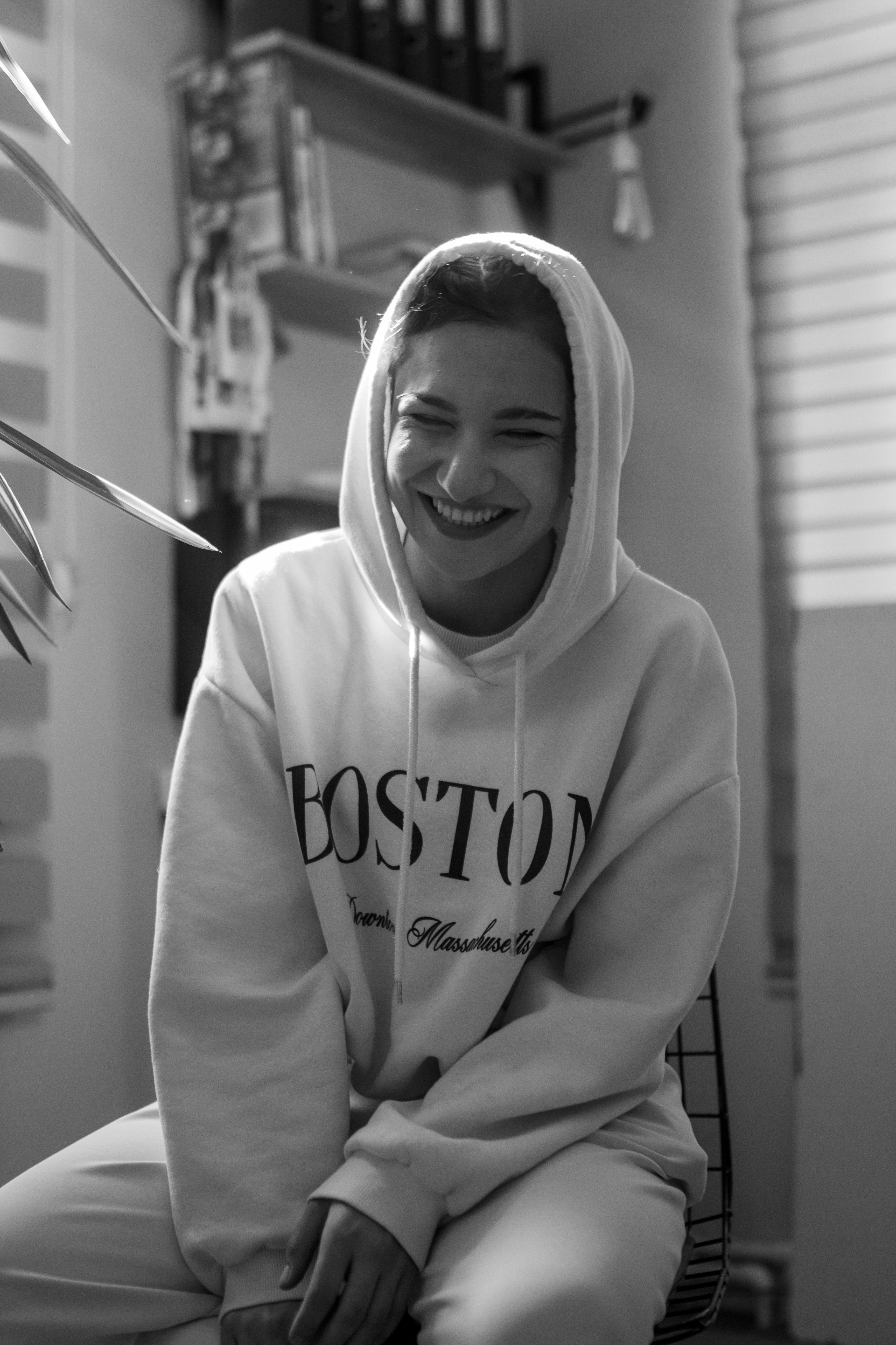 Black and white portrait of a woman in a hoodie smiling warmly indoors.