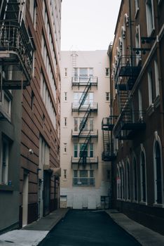 A narrow alley between tall, historic urban buildings featuring fire escapes and architectural details.