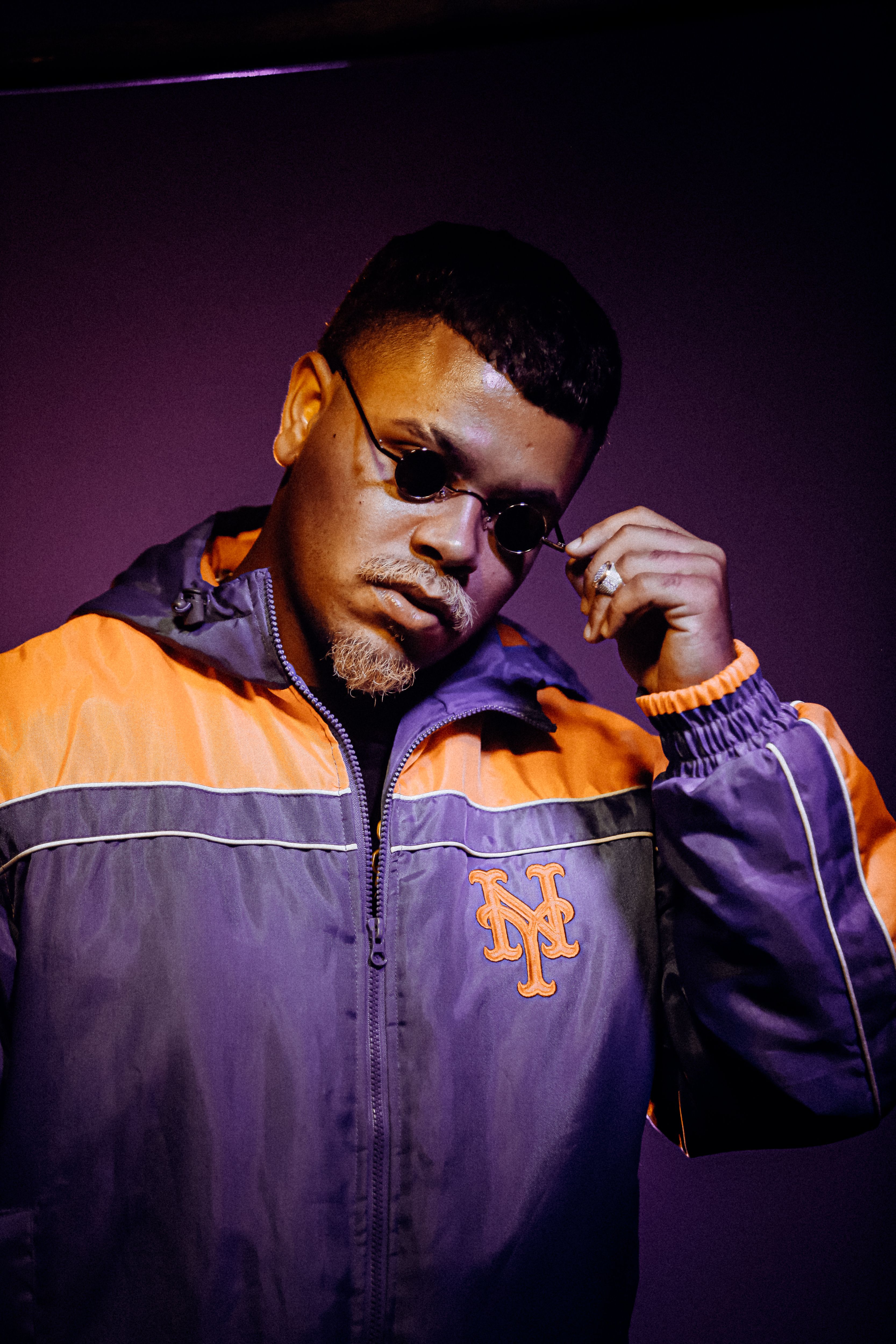 Portrait of a stylish man in a jacket and sunglasses against a vibrant violet background.