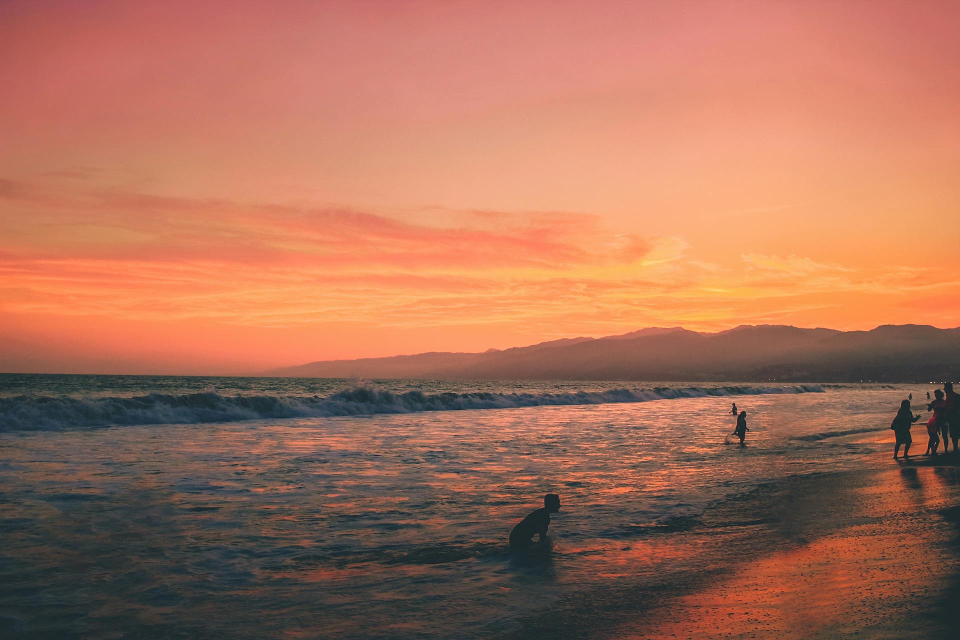 A serene sunset view at Santa Monica beach with silhouettes of people enjoying the ocean.