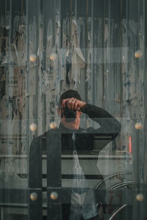 Free Artistic reflection of a person taking a photograph through a glass window in an urban setting. Stock Photo