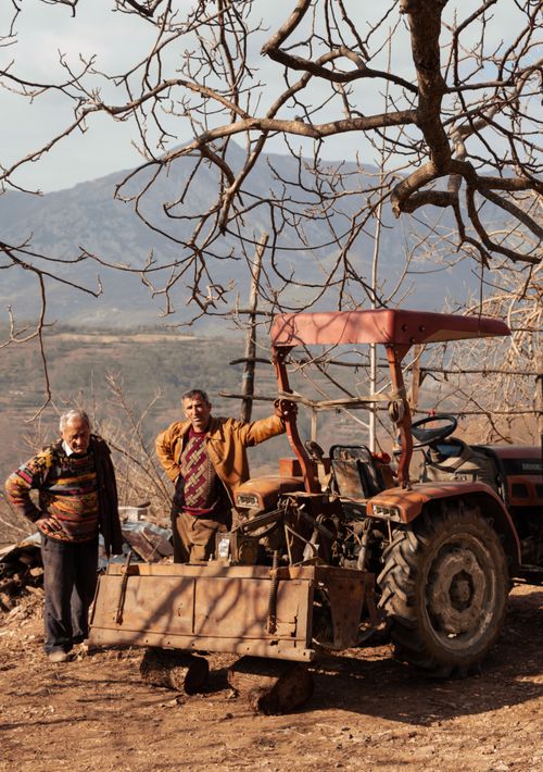 Free Two men standing by a tractor in a rural Albanian landscape, capturing local agriculture. Stock Photo