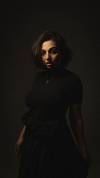 A captivating moody portrait of a woman in a black dress with necklace, captured in a studio setting.
