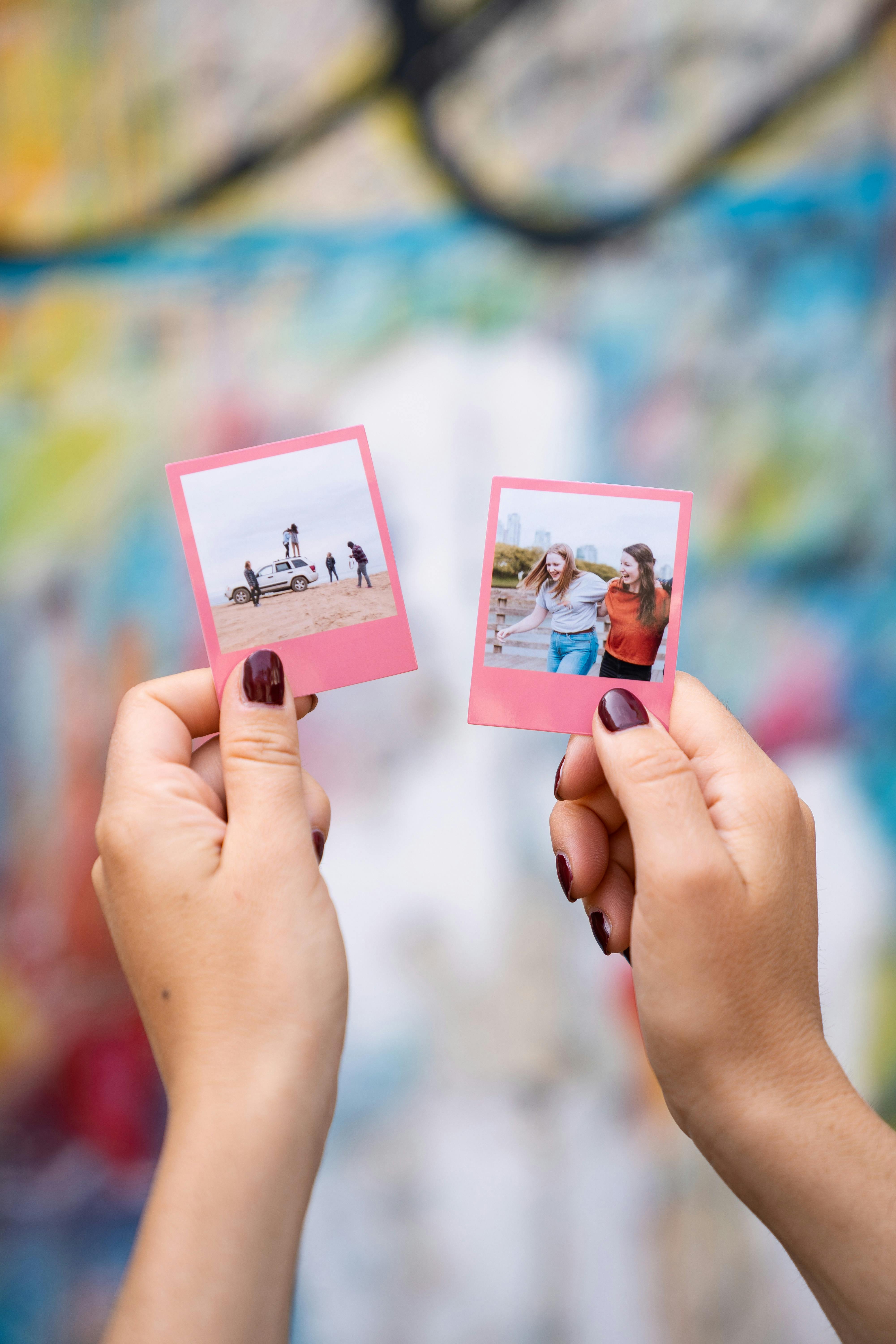 Two hands holding polaroid photos in front of a vibrant, blurred background.