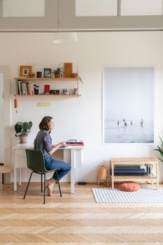 Woman working at a desk in a stylish, minimalist home office with art and plants.
