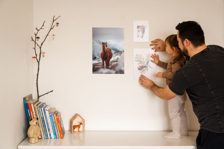 Photo by Squared one on Pexels A father helps his daughter hang pictures on a wall, creating a warm and cozy home environment. - Photo by Squared one on Pexels