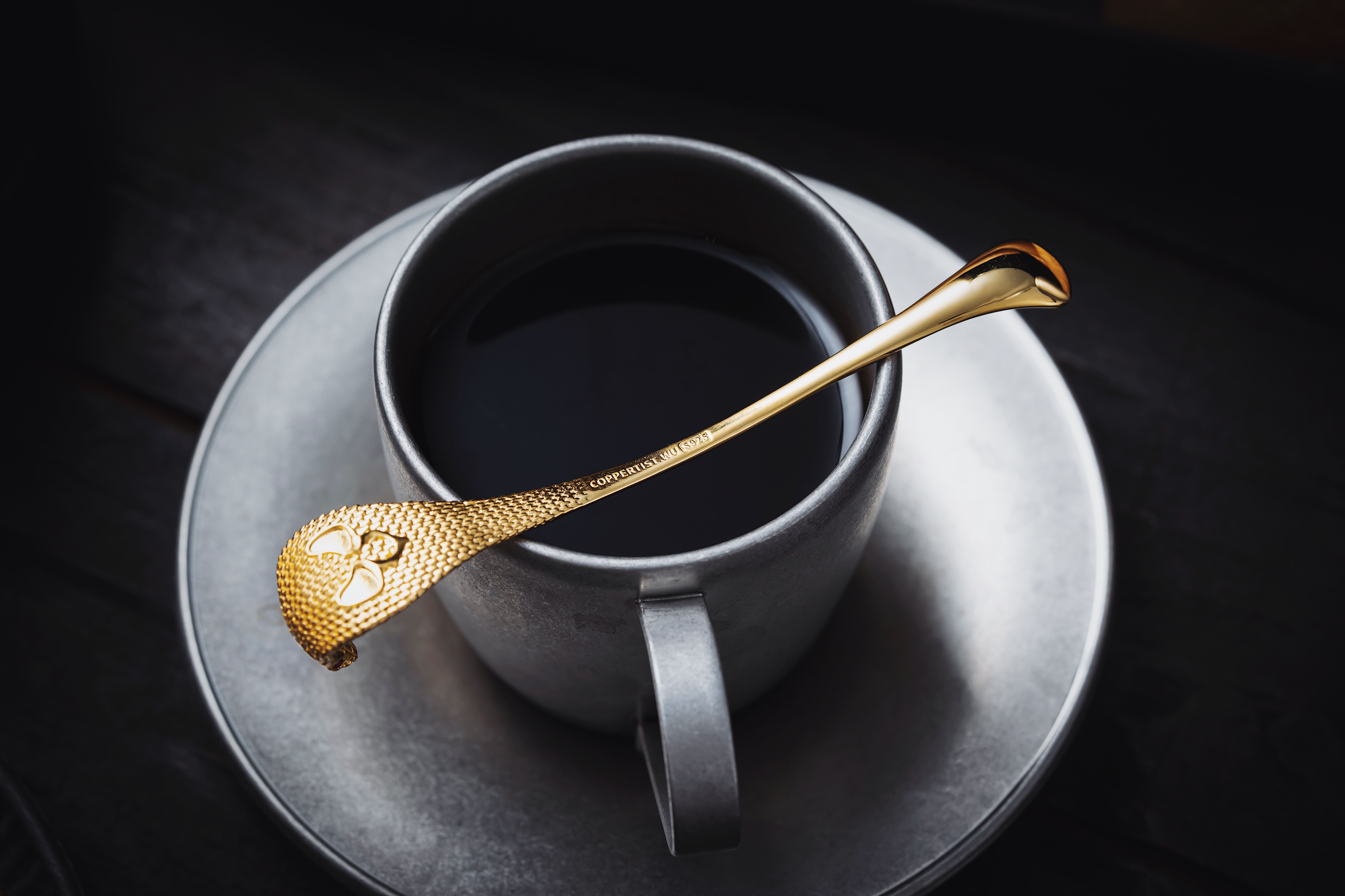 Stylish black coffee in a cup with a golden spoon on a gray saucer, perfect for luxury lifestyle visuals.