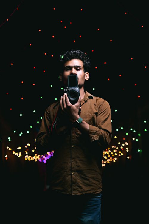 Free Man holding camera with colorful Christmas lights in the background during night time. Stock Photo