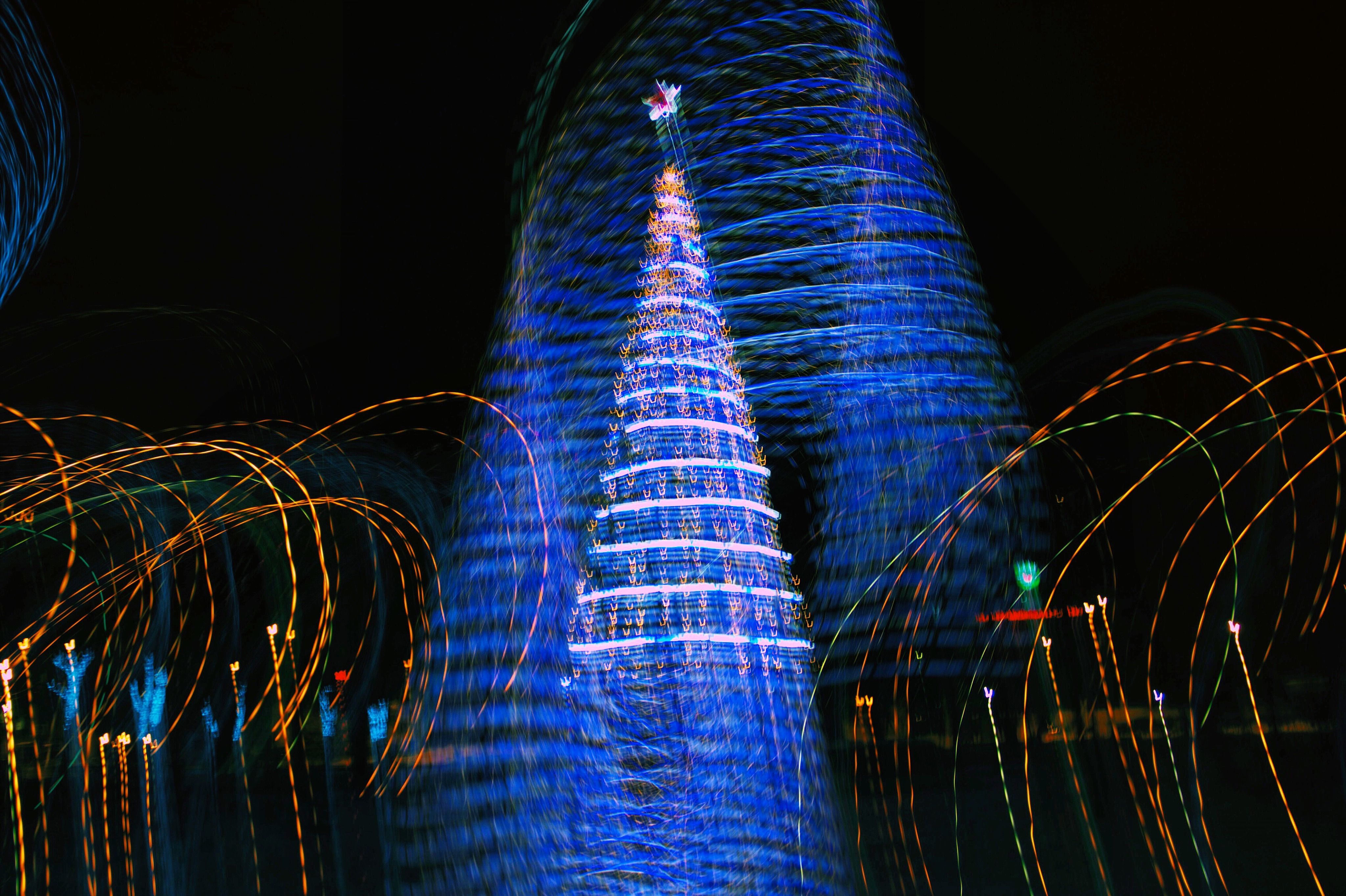 Vibrant abstract image of a Christmas tree with swirling blue and orange lights at night.