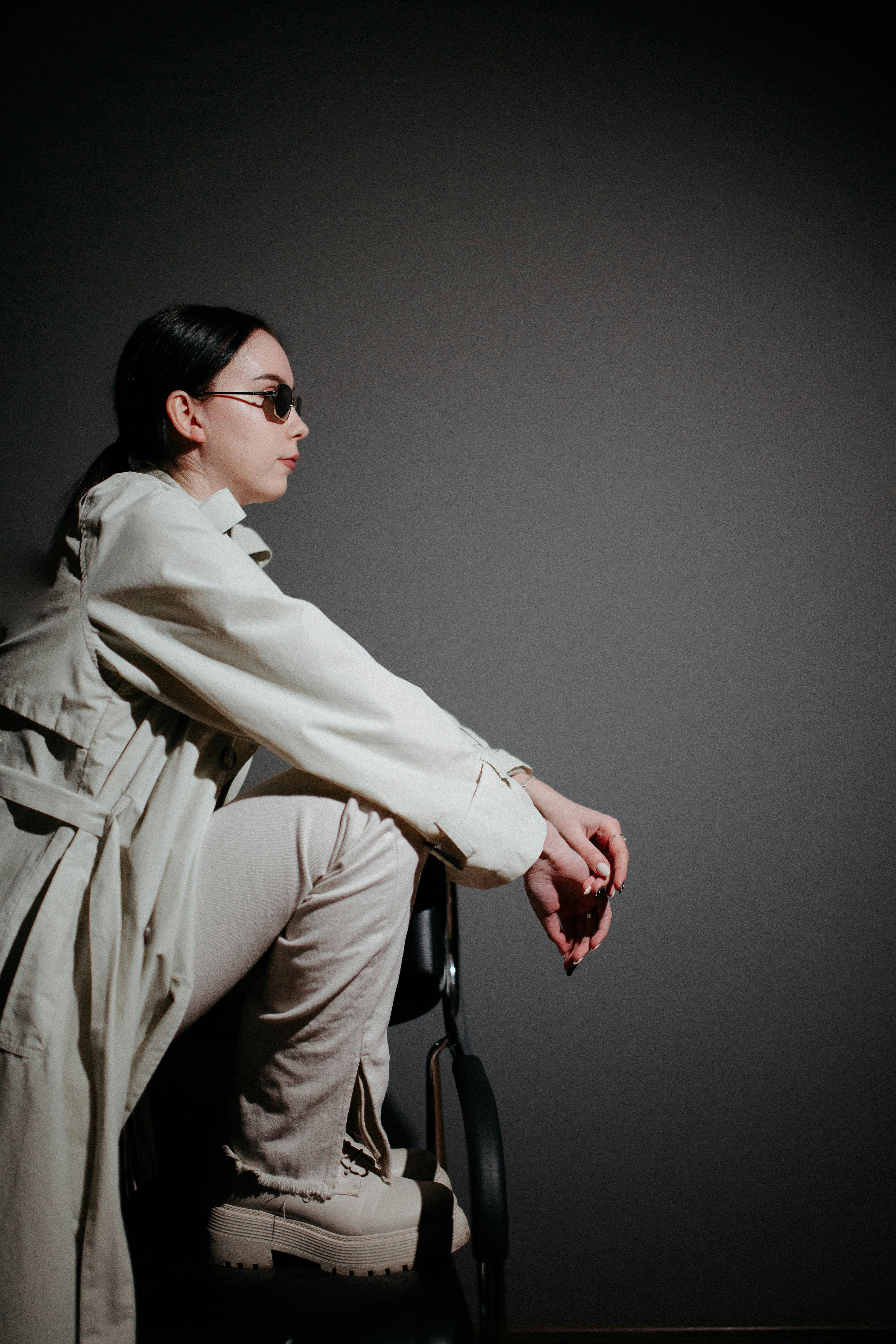 Elegant woman in sunglasses sitting stylishly against a dark studio background.
