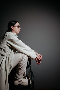 Elegant woman in sunglasses sitting stylishly against a dark studio background.