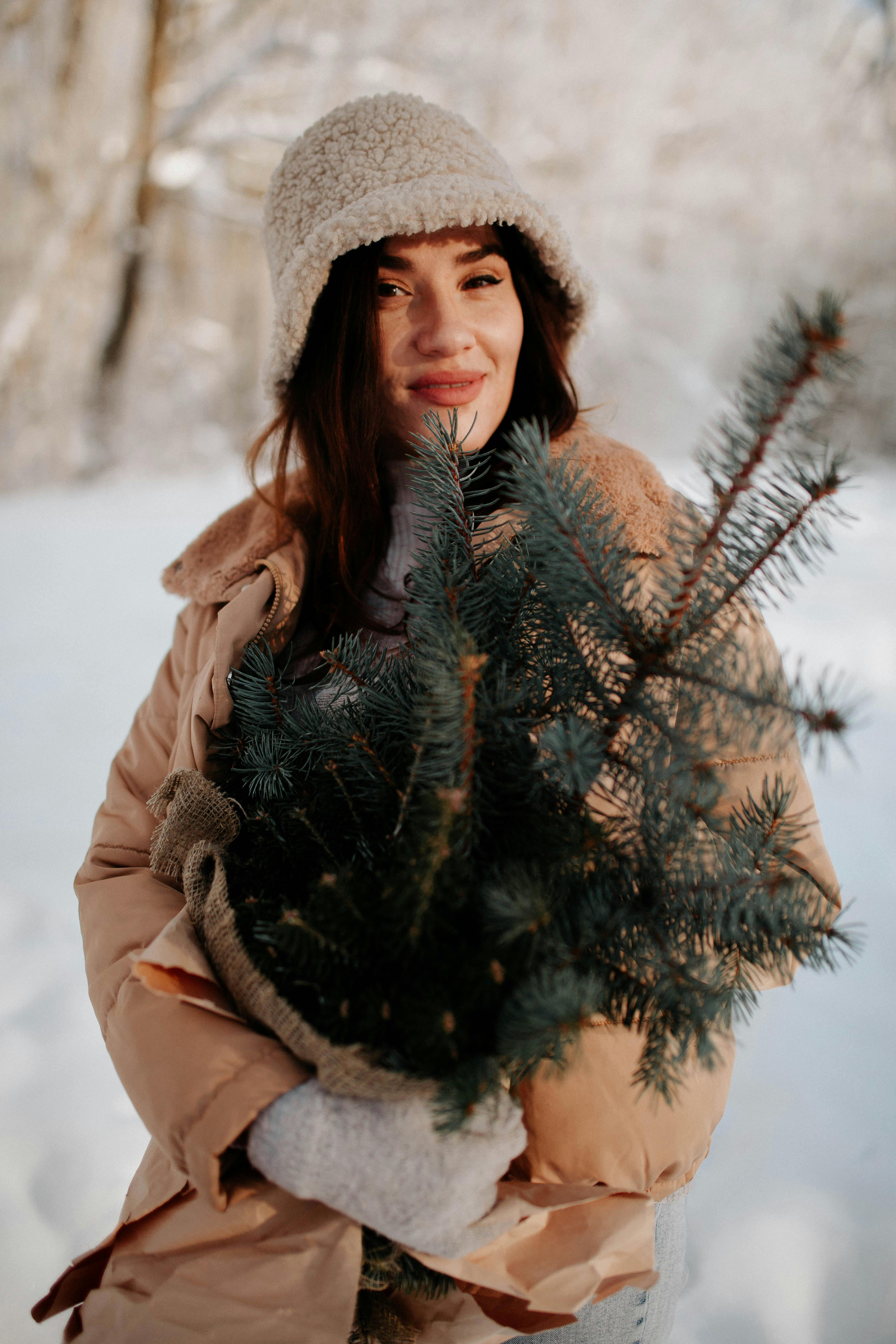 Young woman warmly dressed holding evergreen branches in snow, radiating winter joy.