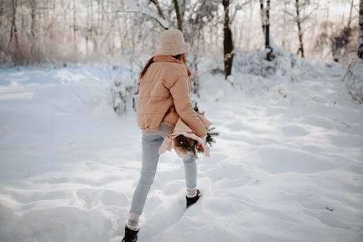 Woman walking in a snowy forest, carrying an evergreen branch during winter.