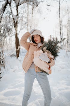 Young woman in winter outfit holding evergreen branches in snowy forest setting.