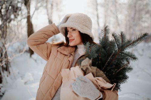 Free Woman in warm clothing holding fir branches in a snowy forest setting. Stock Photo