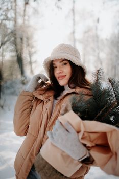 Young woman in warm clothing holding a Christmas tree outdoors in winter.