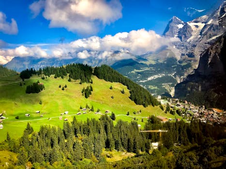 Picturesque alpine village surrounded by lush greenery and scenic mountains under a vibrant blue sky.