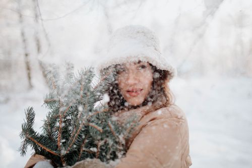Free A woman in winter clothing holding pine branches on a snowy day. Stock Photo