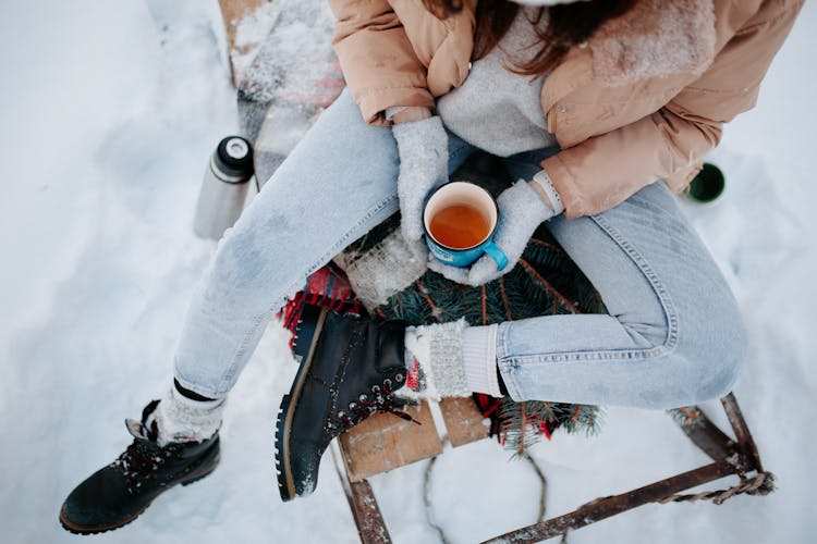 Woman Sitting On Sleight With Tea On Winter Day