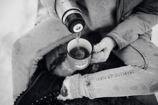 A person pours hot drink into a cup in a snowy winter setting.