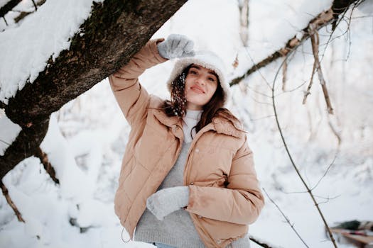 Woman in warm clothing standing under snowy branches in a winter forest.