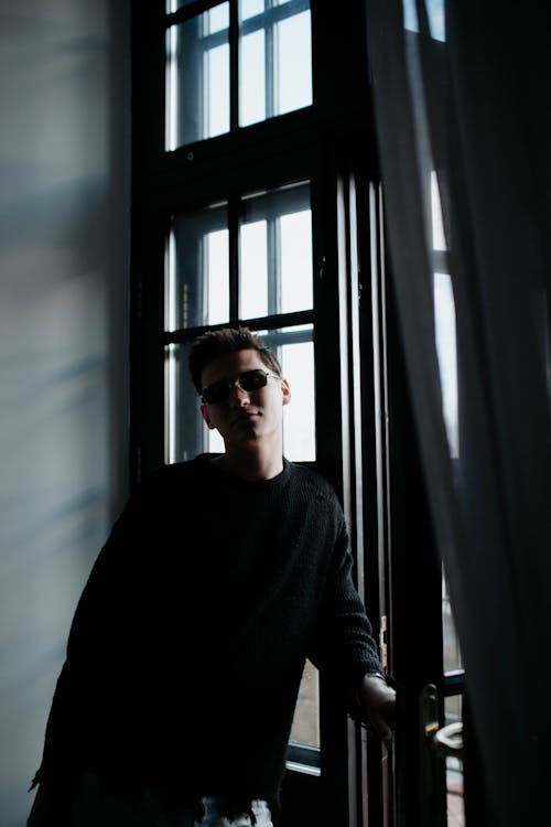 Young Man Wearing Sunglasses Posing against a Window with Curtain