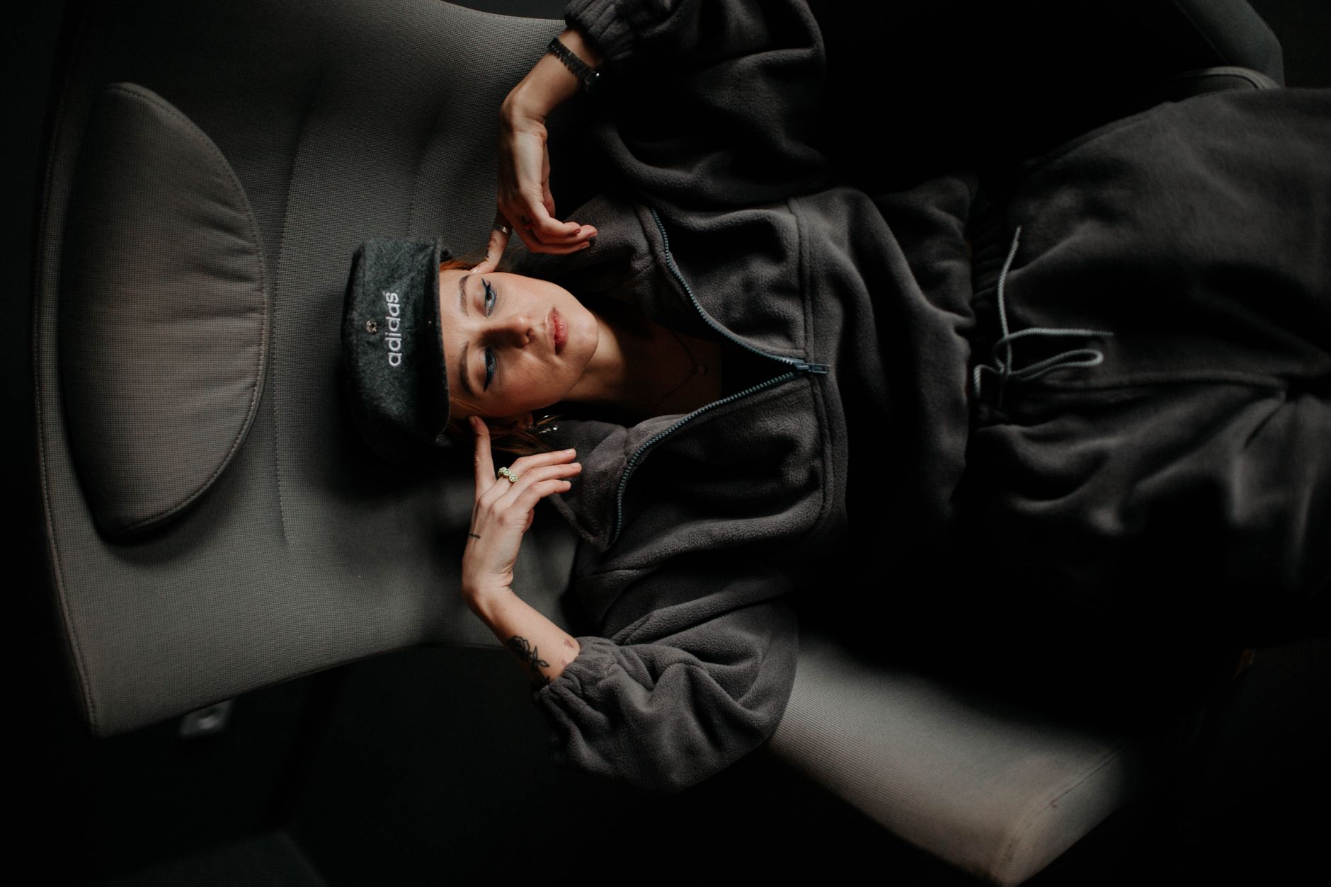 A young woman wearing a hoodie and cap lounges comfortably in an armchair, exemplifying relaxation and style.