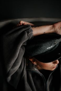 A woman in a sweatshirt and cap relaxing indoors with a moody tone.