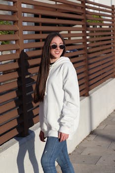 Woman in white hoodie and sunglasses smiles while standing outdoors in Córdoba.