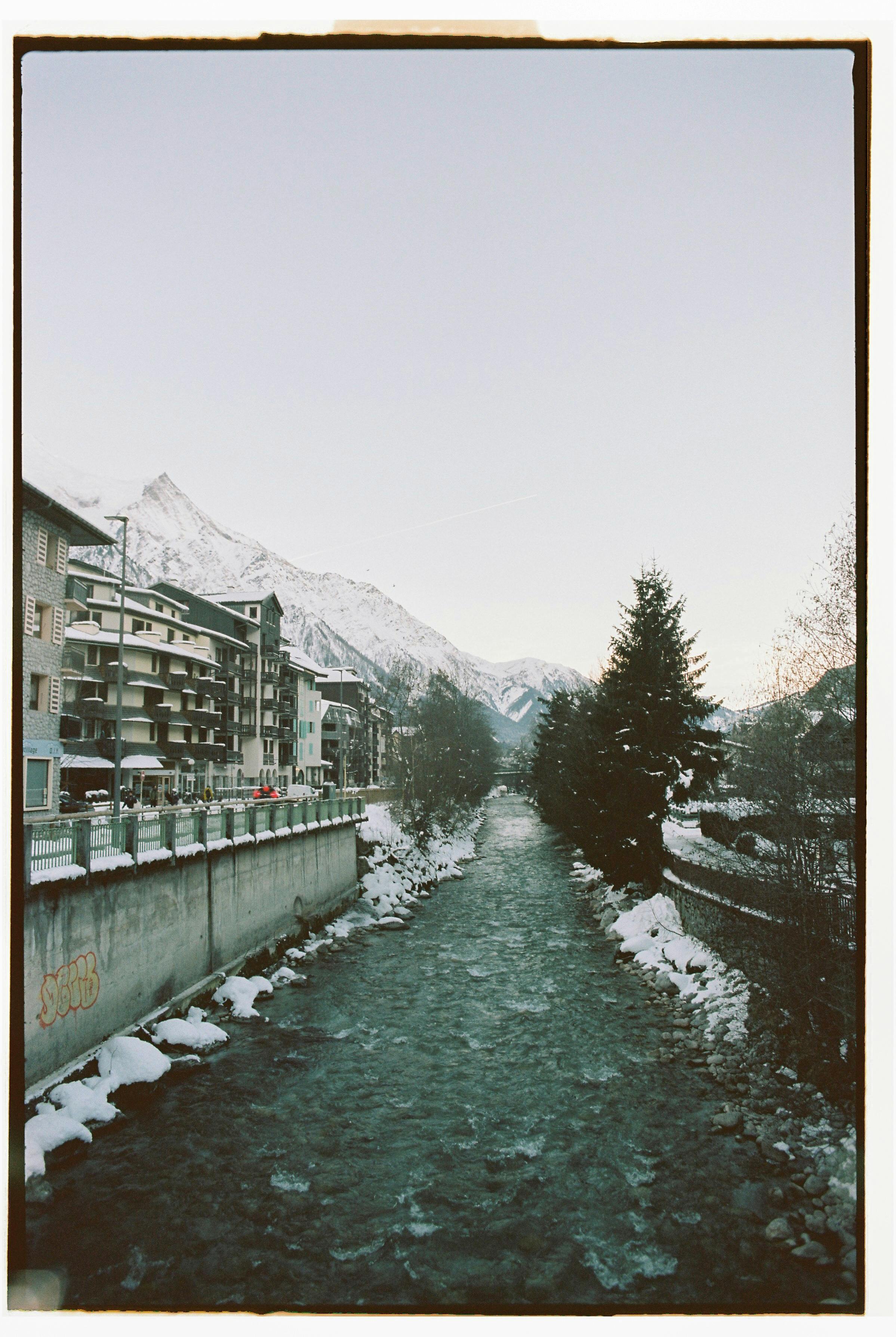 Snow-covered town of Chamonix with a flowing river and mountain backdrop during winter.