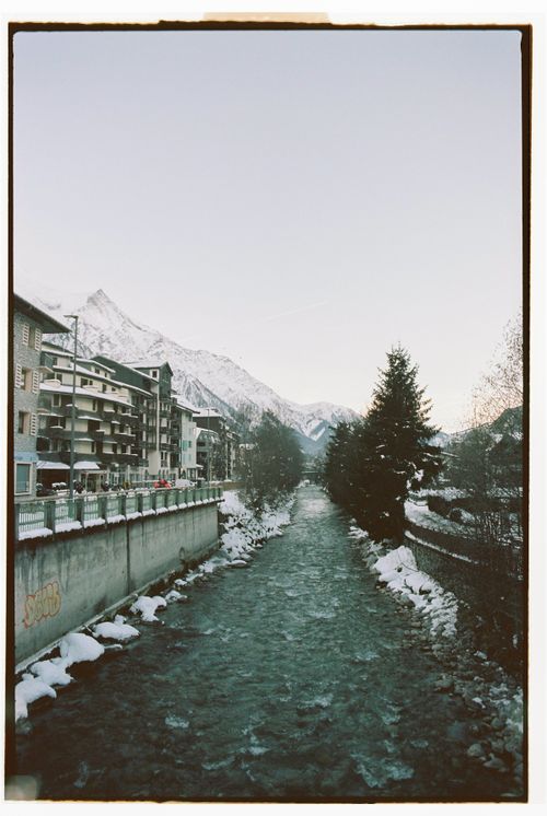 Free Snow-covered town of Chamonix with a flowing river and mountain backdrop during winter. Stock Photo