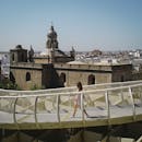 一位女士在塞维利亚的大都会遮阳伞下散步，背景是一座历史悠久的教堂