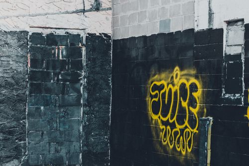 Free Yellow graffiti art on a black brick wall in an urban setting. Stock Photo