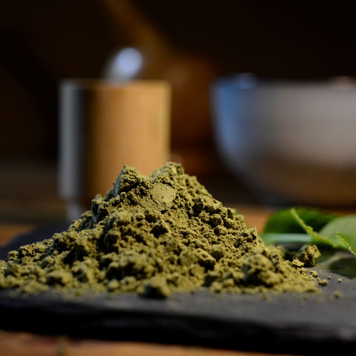 Čistý kratomový prášek a listy Mitragyna speciosa na tmavém podkladu